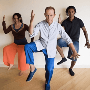 A man and two women are dancing in front of the wall.