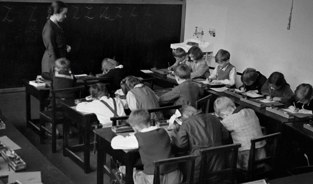A group of students sitting at desks in front of blackboard.