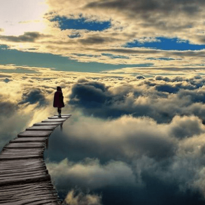 A person walking on a bridge over clouds.